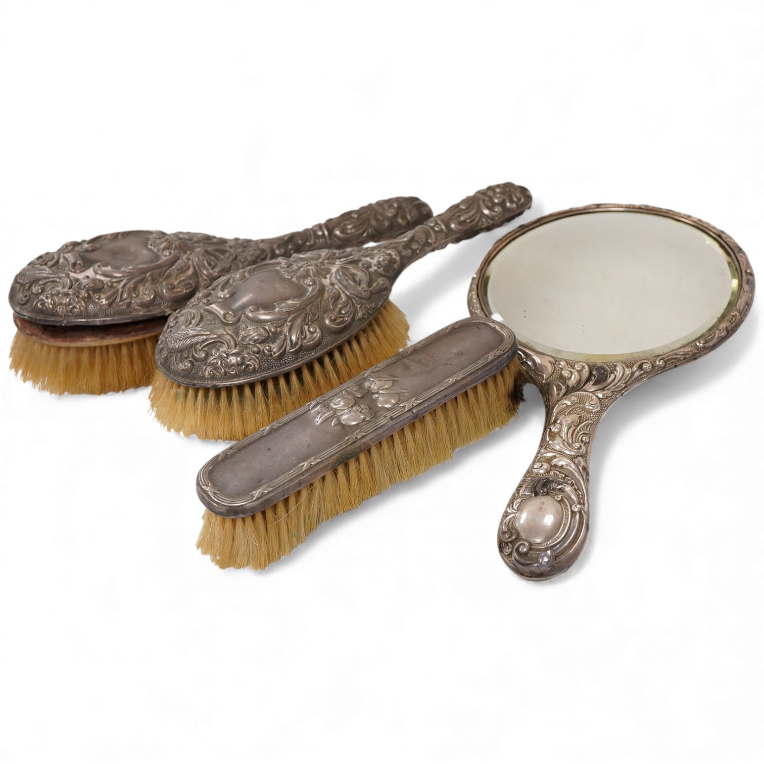Four assorted early 20th century repousse silver mounted dressing table items to include a hand mirror, two hair brushes and a clothes brush(a.f.).